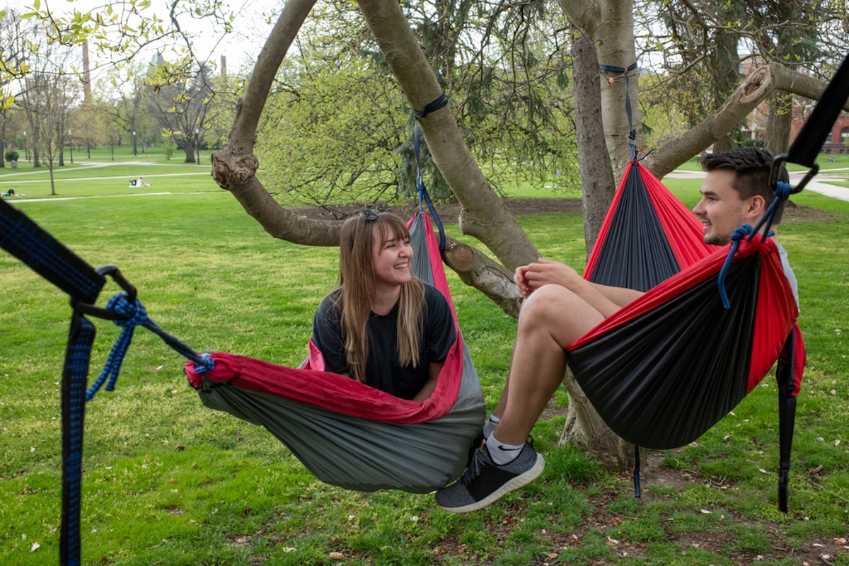 Two students sitting in hammocks hanging from a tree on the Oval.