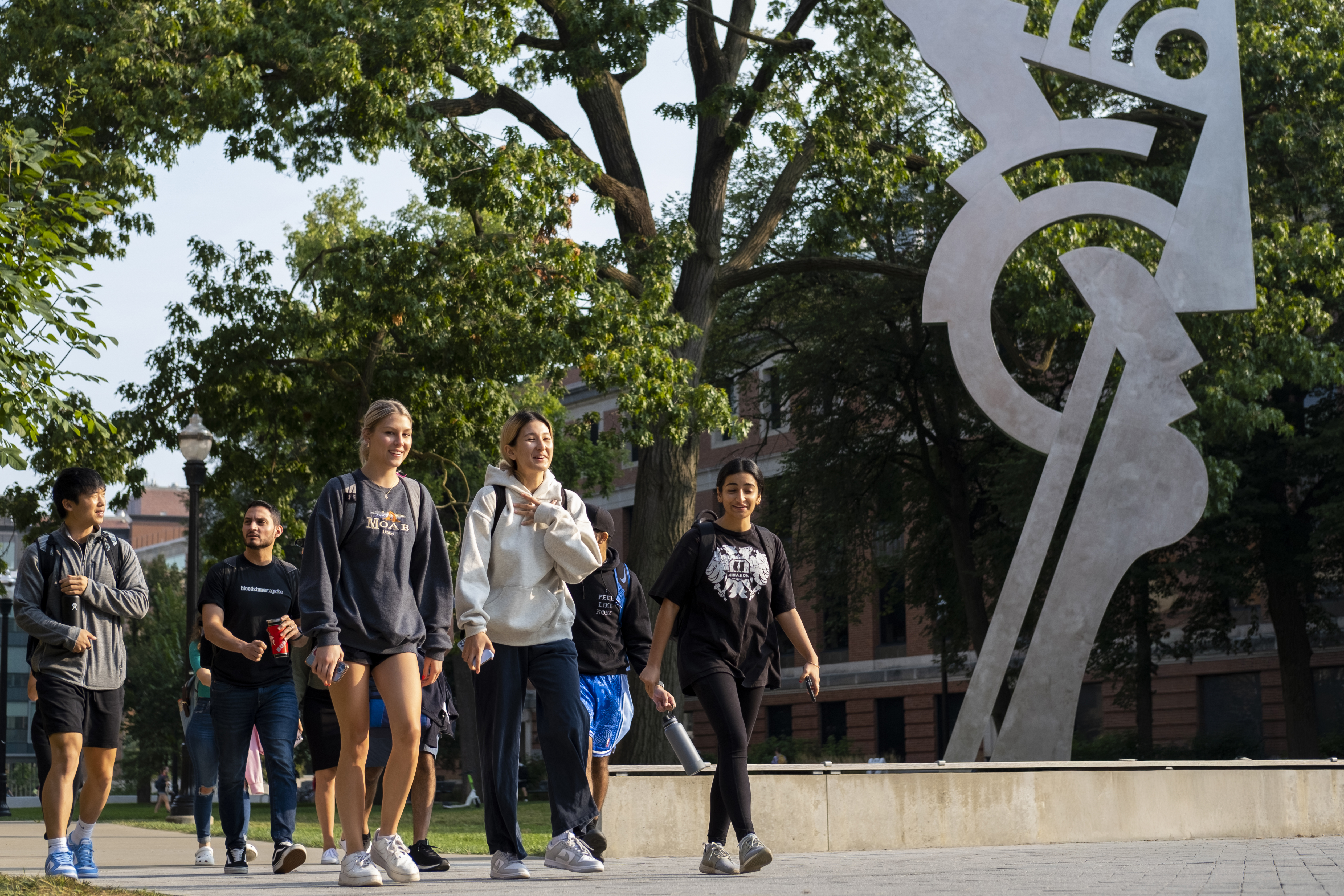 Group of students walking across campus in front of a sculpture