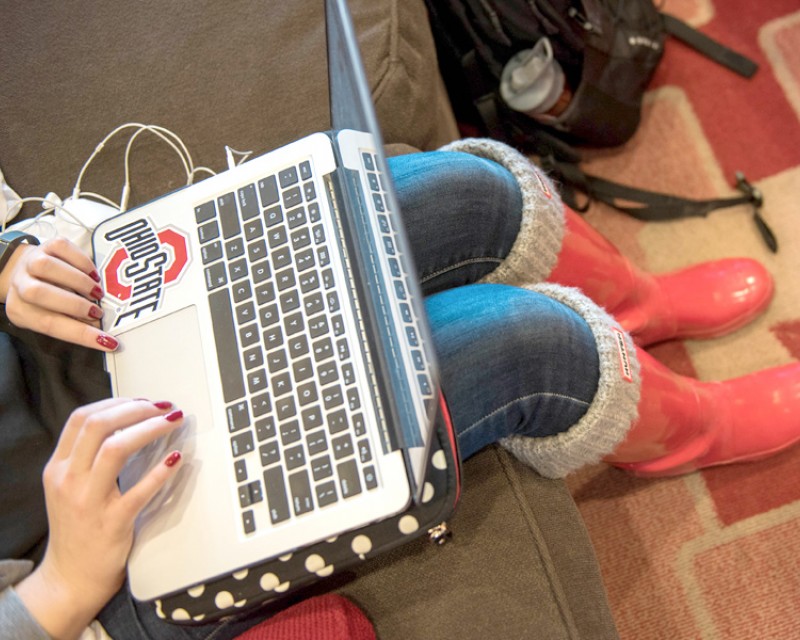 A person typing on a laptop. The laptop has a large sticker of the Ohio State University logo below the keyboard.