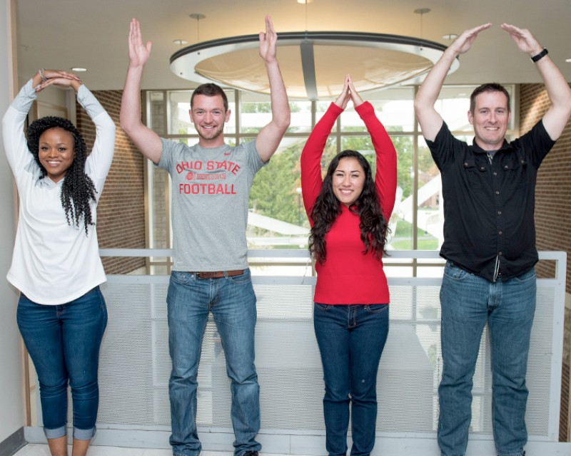 Four students standing up and spelling O-H-I-O with their arms.