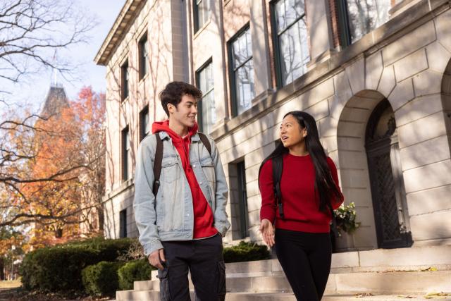 Two students conversing on a fall day in front of an academic building